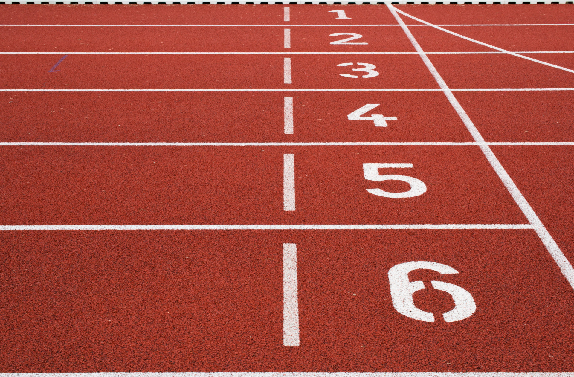 Červená atletická dráha s bielymi čiarami a číslami 1 až 5, šikmý pruh vpravo.